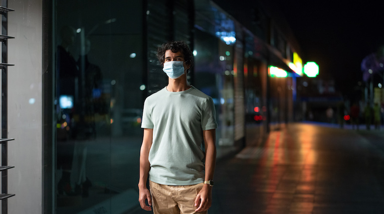 man standing on a street wearing a face mask during night curfew